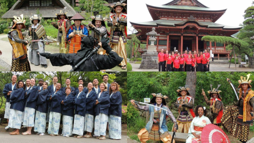 Esta é uma montagem de quatro fotos que mostram um grupo de pessoas em diferentes cenários e trajes tradicionais japoneses. As expressões são de alegria e entusiasmo. No canto superior esquerdo, um grupo de seis homens está vestido com armaduras de Samurai completas, incluindo capacetes e espadas. Eles posam de forma dinâmica em uma área externa com casas de estilo rústico ao fundo. À frente deles, de costas para a câmera, uma figura vestida inteiramente de preto como um Ninja faz um gesto dramático. No canto superior direito, o grupo (homens e mulheres) aparece usando uniformes vermelhos idênticos. Eles estão posicionados à frente de uma imponente construção no estilo clássico japonês de madeira vermelha, com telhados de múltiplas camadas e uma lanterna de pedra ao lado.
No canto inferior esquerdo, o grupo posa perfilado, todos vestindo quimonos iguais em tons de azul escuro e branco. Eles estão sorrindo para a foto em um ambiente arborizado. No canto inferior direito, uma cena festiva onde alguns integrantes aparecem novamente com armaduras de Samurai, empunhando katanas. No centro, uma mulher sorridente, sentada em um banco, veste um quimono branco com detalhes florais e segura uma sombrinha vermelha aberta. O fundo é composto por muros de pedra e vegetação.